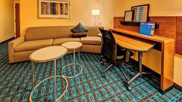 A hotel room with a sofa, two small round tables, a desk, and a patterned carpet.