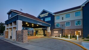 A hotel with a modern design, featuring a prominent entrance with a covered area and a sign that reads "HOMEWOOD SUITES by Hilton".