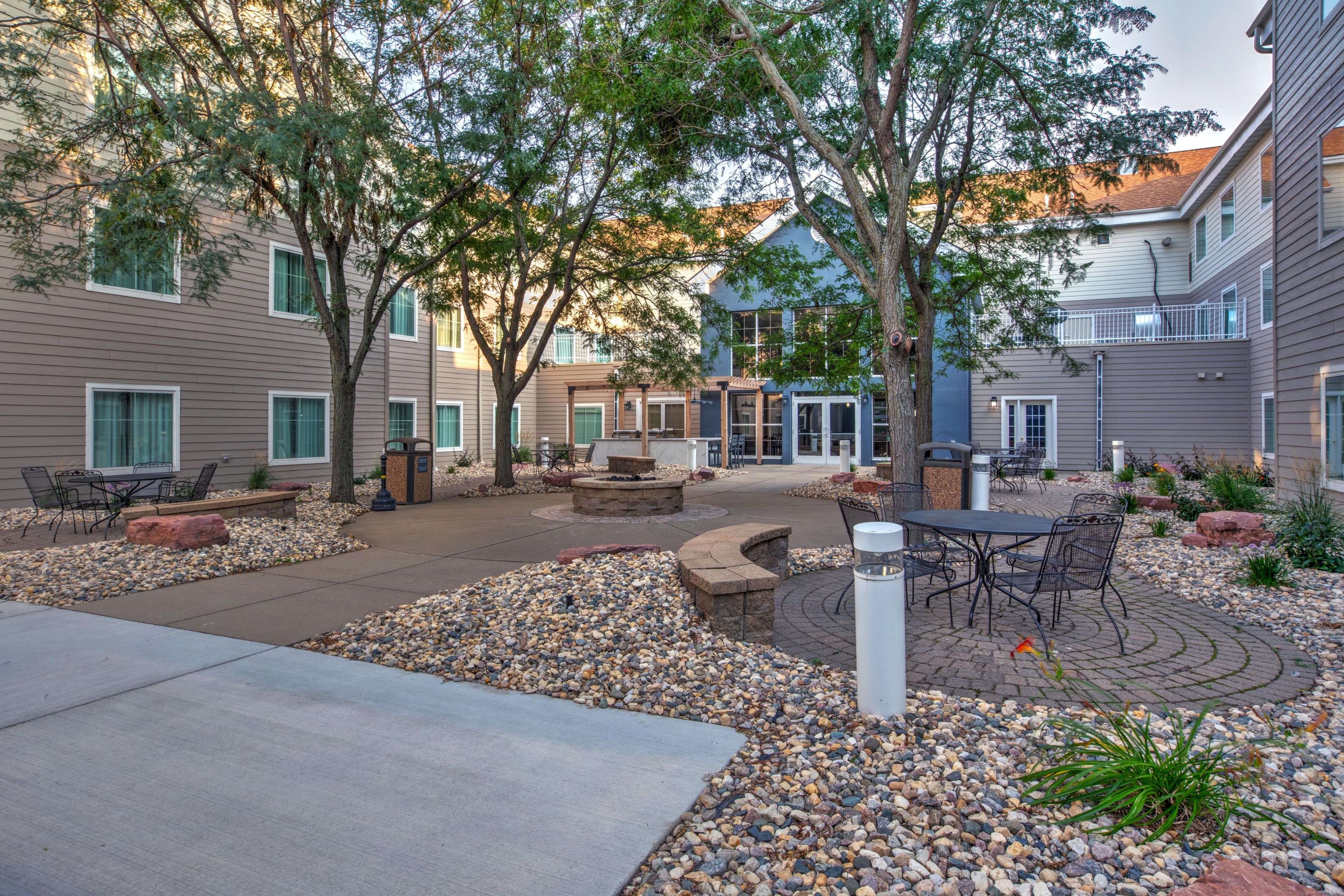 Un patio con mobiliario exterior, una chimenea y un edificio con múltiples ventanas y balcones.