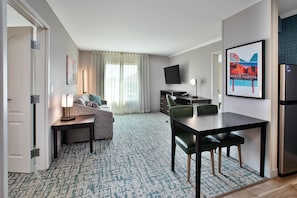 Una habitación de hotel con una cama, un escritorio, una silla, un televisor y un cartel de bienvenida enmarcado.
