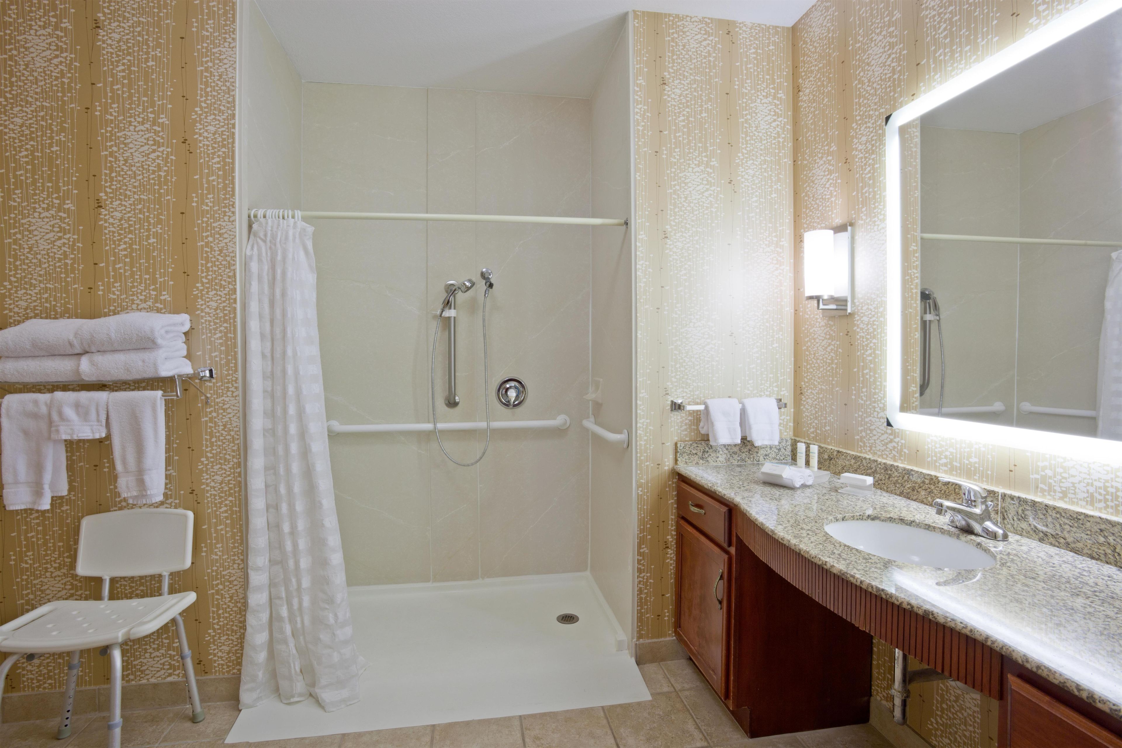 A bathroom with a shower, a sink, a mirror, and a chair.