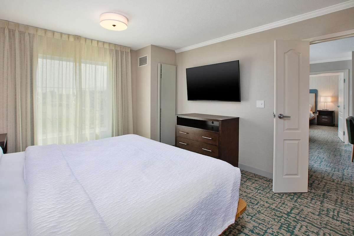 A hotel room with a large bed, a flat-screen TV mounted on the wall, a wardrobe, and a door leading to another room.