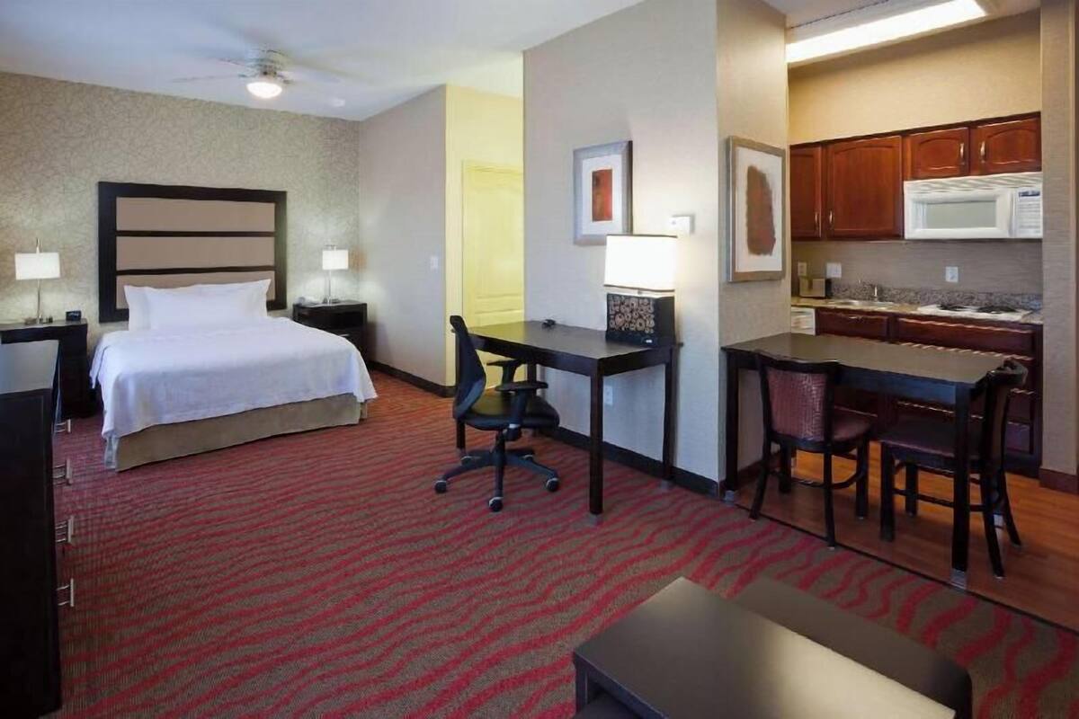 A hotel room with a bed, desk, chair, and kitchenette.