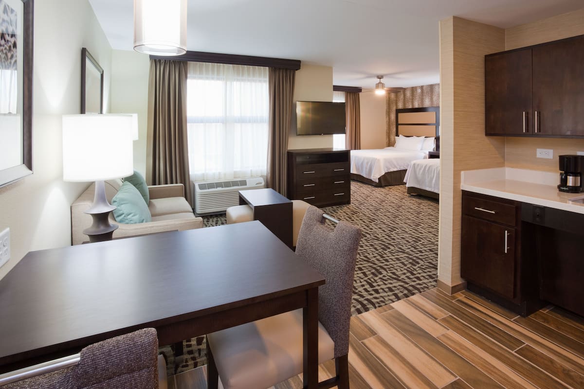 A hotel room with a dining area, a bed, a TV, and a kitchenette.