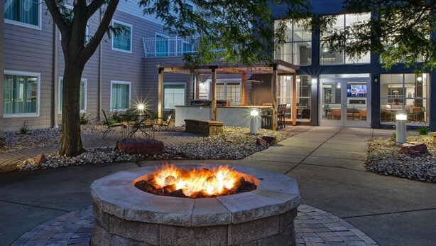 A fire pit in a circular stone structure, surrounded by a paved area with a pergola and outdoor seating.