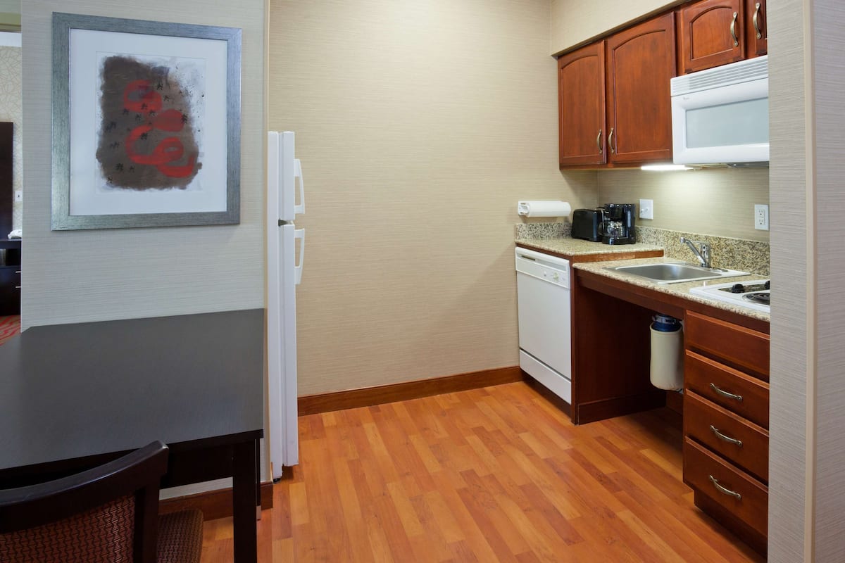 A compact kitchen with wooden cabinets, a microwave, a dishwasher, and a granite countertop.
