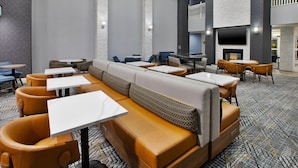 A modern hotel lobby with a central seating area, multiple tables, and a fireplace.