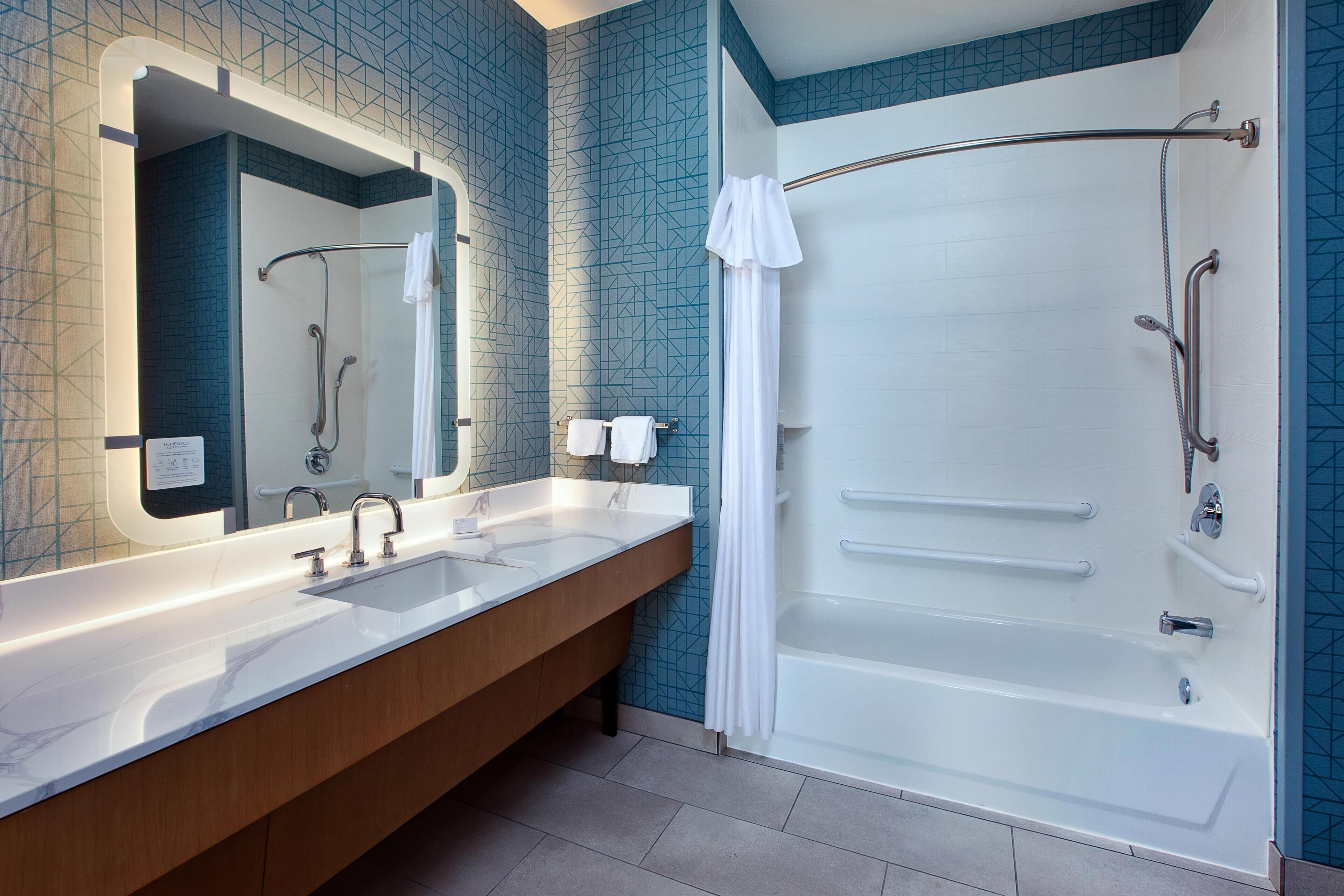 Um banheiro moderno com bancada com duas pias, um espelho grande, chuveiro com box de vidro e azulejos estampados em azul.