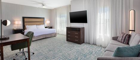 Quarto de hotel com cama, escrivaninha, poltrona, cômoda, televisão e sofá.