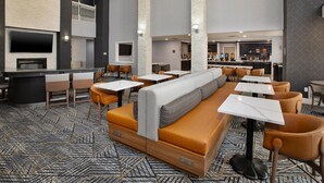 A modern hotel lobby with a high ceiling, a fireplace, a bar area, and seating arrangements.