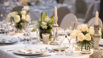 Mesa dispuesta para un evento formal, con manteles blancos, cristalería y centros de mesa florales.