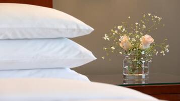 Una cama con almohadas blancas y un florero con flores sobre una mesita de noche.