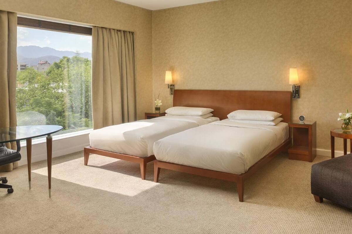 Une chambre d’hôtel avec deux lits, un bureau, une chaise et une vue sur les montagnes.