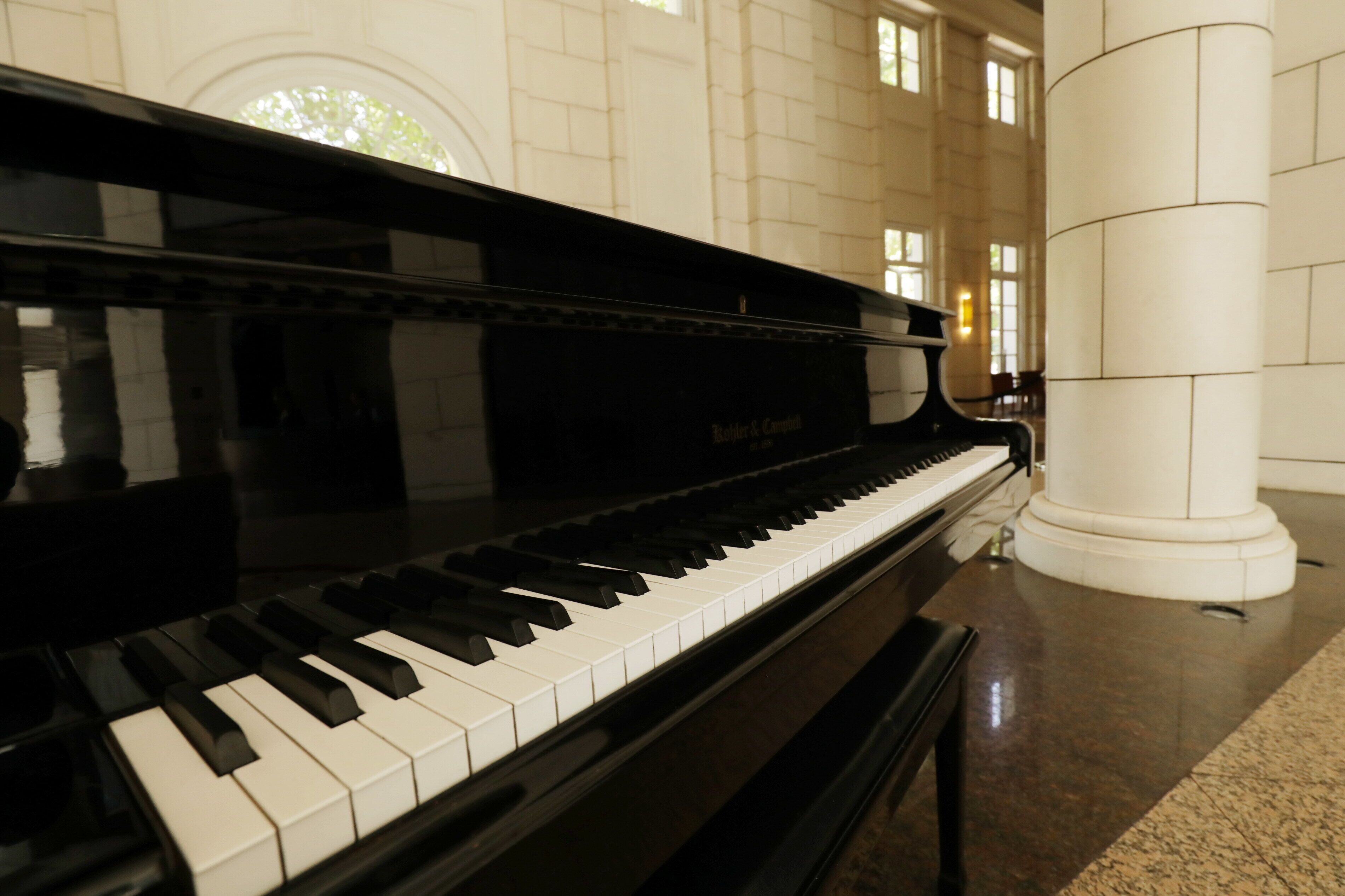 Un piano de cola en un amplio salón con techo alto y ventanas grandes.