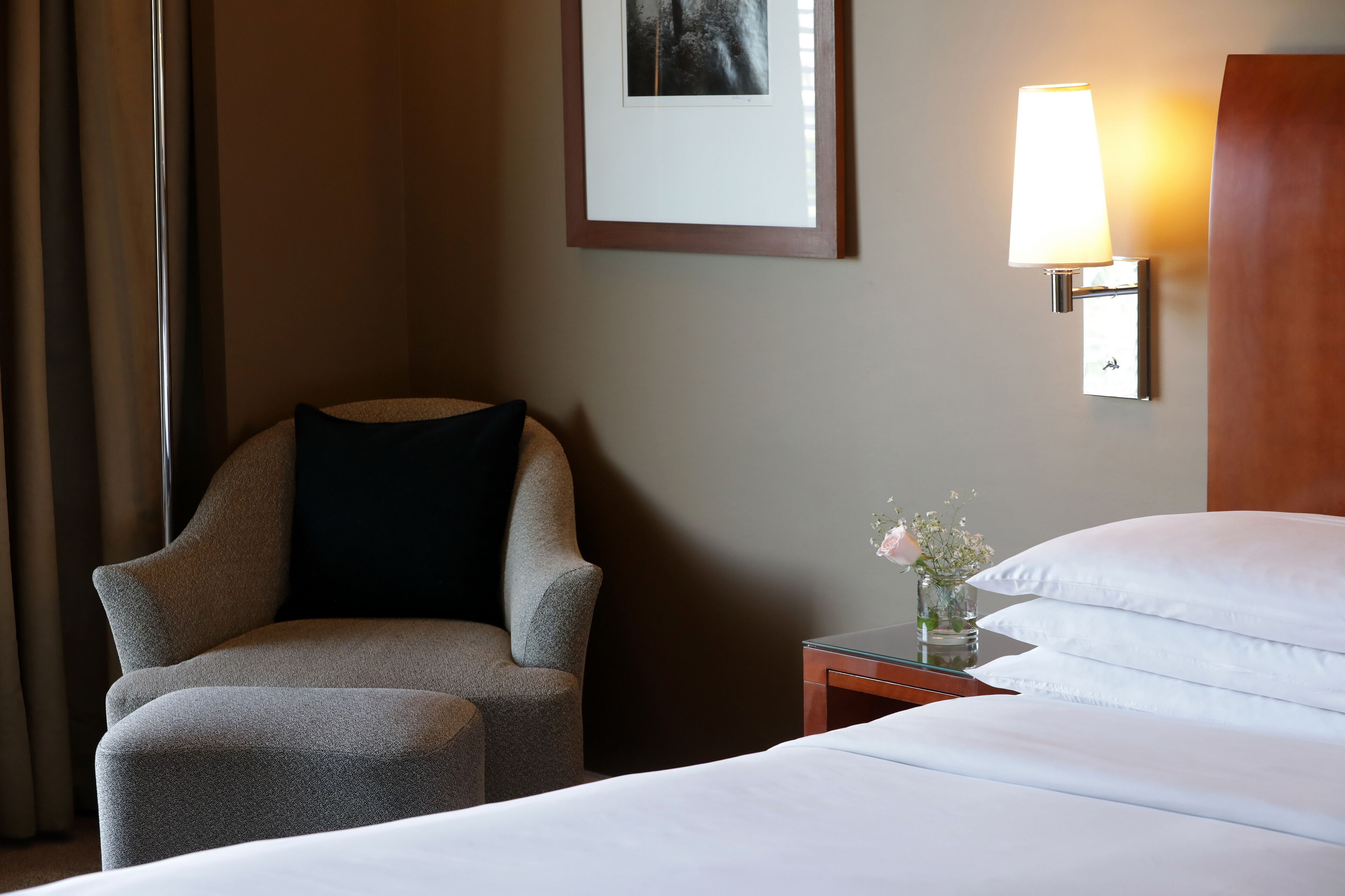 A hotel room with a bed, a chair, a nightstand with a lamp, and a framed picture on the wall.