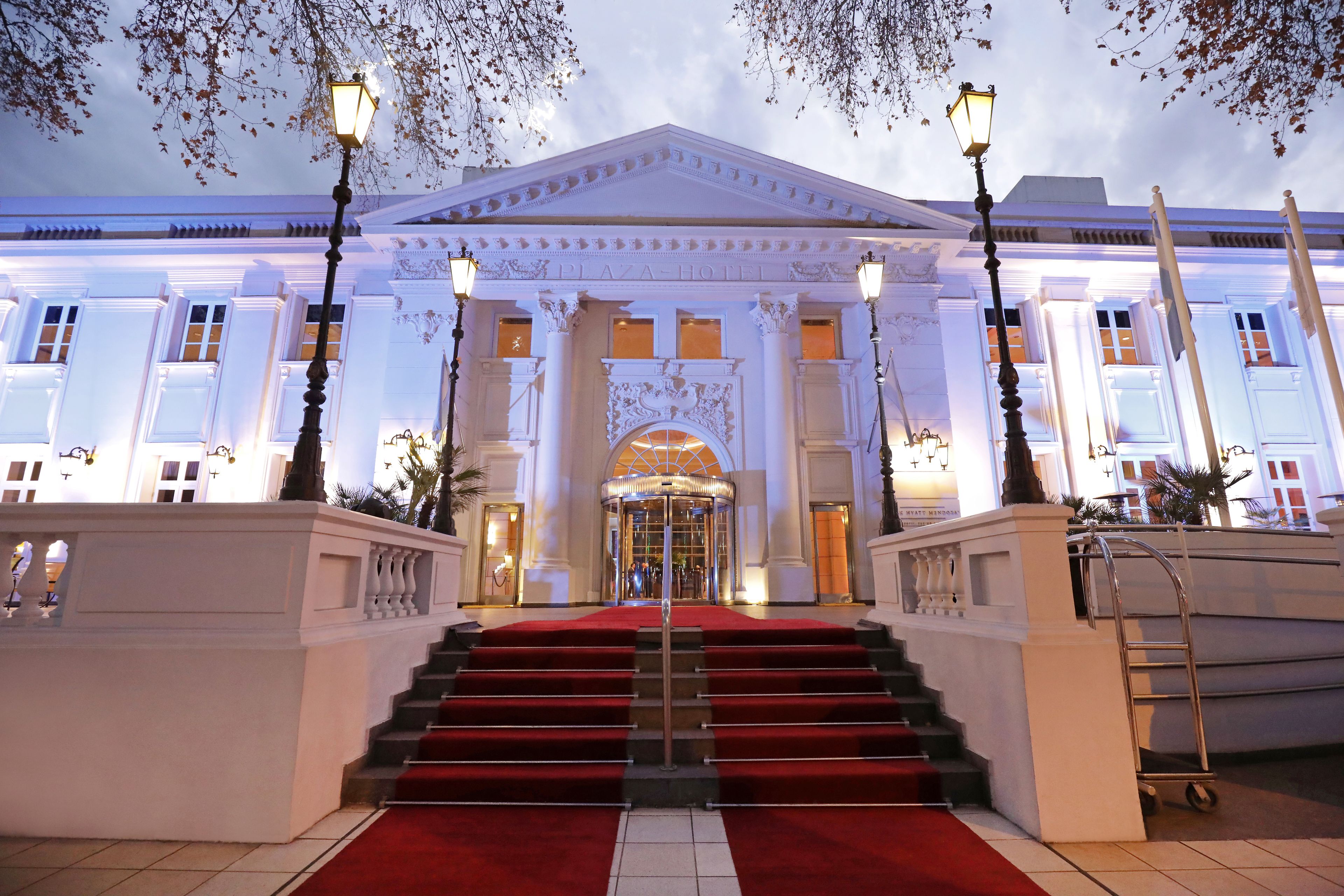 Une entrée imposante, avec un tapis rouge menant à un escalier, flanqué de colonnes et agrémenté de luminaires décoratifs.