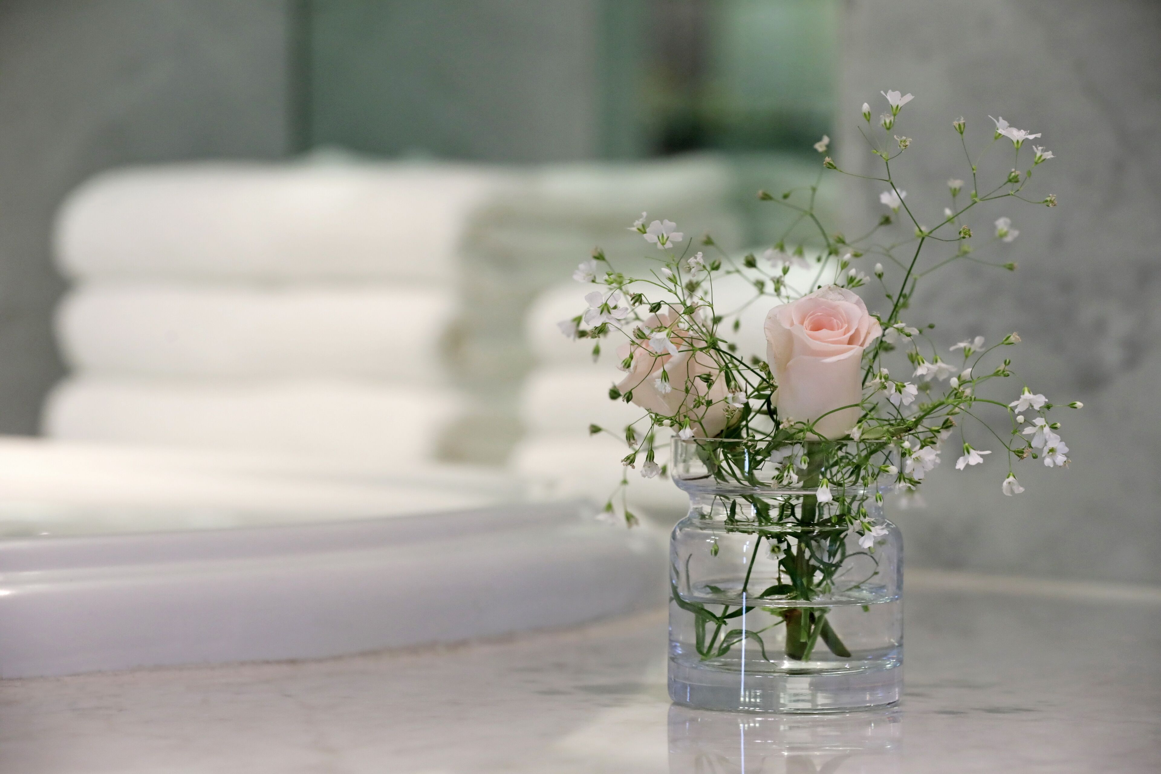 Um vaso de vidro transparente com uma rosa rosa e flores brancas sobre uma superfície de mármore.