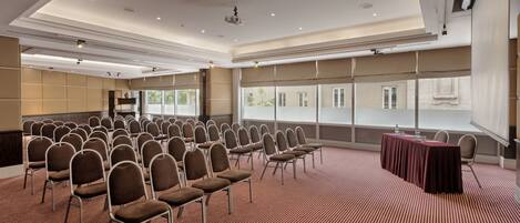 A conference room with rows of chairs, a table with a tablecloth, and large windows.