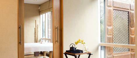 Una habitación de hotel con una cama, una mesita con un jarrón de flores y un ventanal con un diseño de celosía de madera.