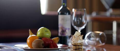 A dining table with a plate of fruit, a bottle of wine, and a glass of wine.
