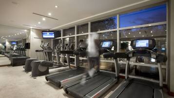 A gym with treadmills, ellipticals, and stationary bikes, with large windows and a digital display.