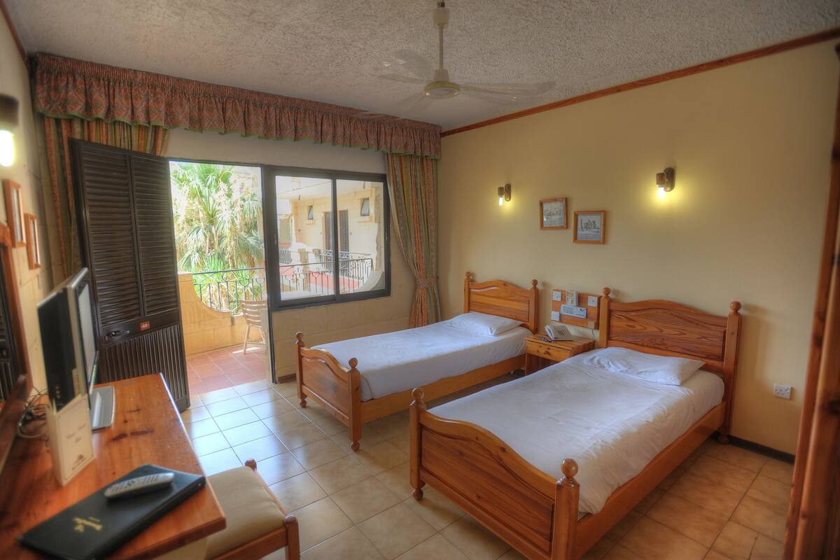 A bedroom with two wooden beds, a desk with a TV, and a ceiling fan.