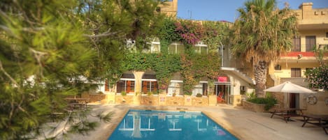 Piscina com borda de pedra, rodeada por um terraço com bancos e guarda-sóis.