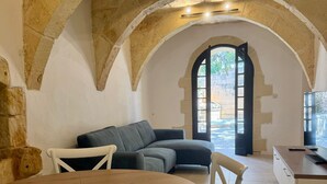 Un salon chaleureux avec un plafond en forme d’arc en pierre, un canapé, une table à manger avec des chaises, et une vue sur un espace extérieur accessible par un passage en arc.