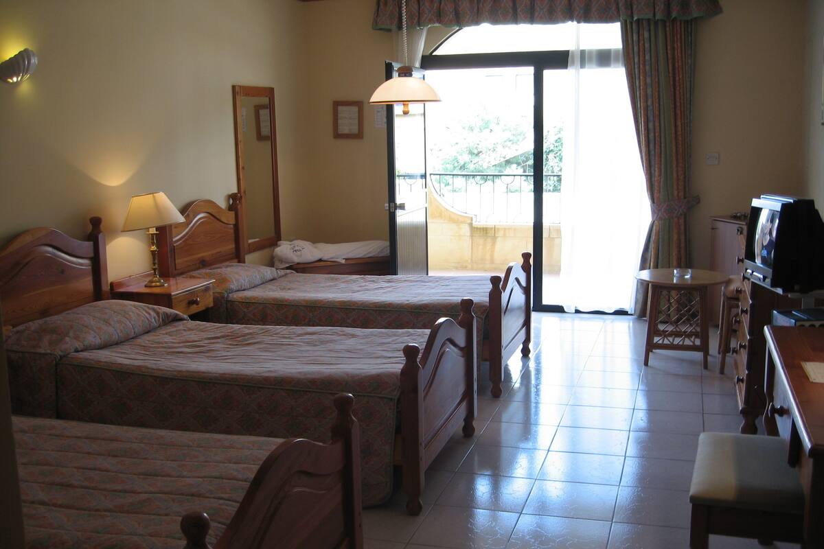 A hotel room with two wooden beds, a desk with a television, and a balcony with a view.