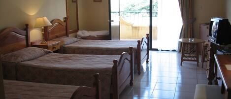 A hotel room with two wooden beds, a desk with a television, and a balcony with a view.
