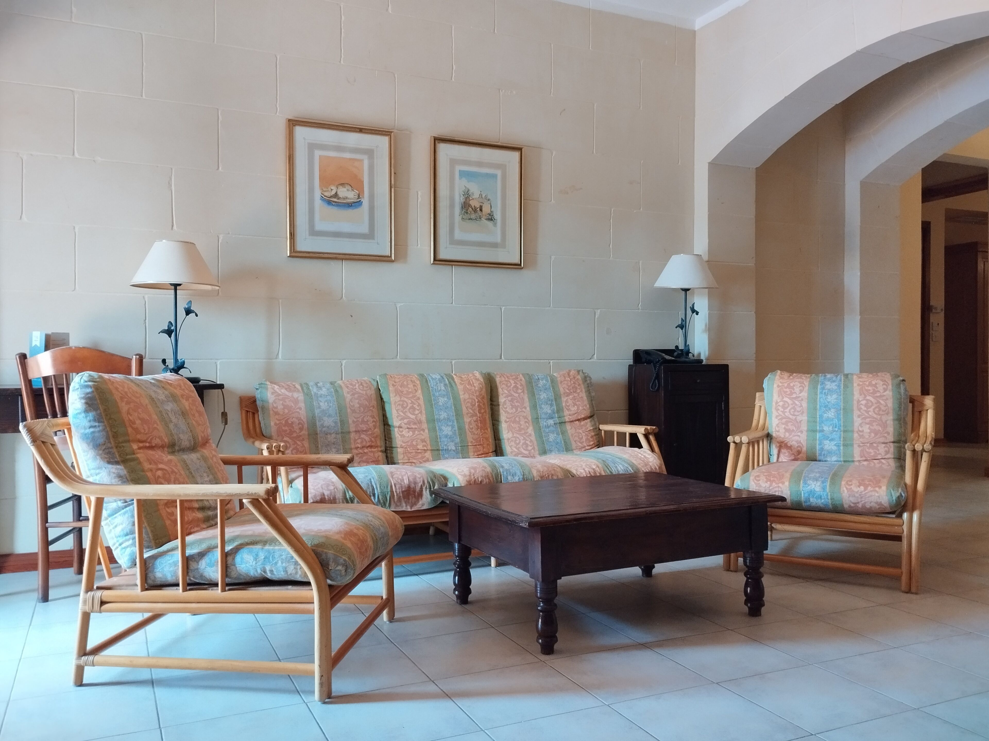 A living room with a sofa set, two armchairs, a coffee table, and two lamps. There are two framed pictures on the wall.