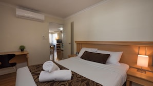 A hotel room with a bed, a desk, a chair, a TV, and an air conditioning unit.