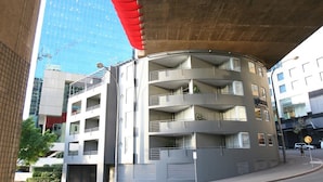A multi-story building with balconies, a curved facade, and a large overpass above.