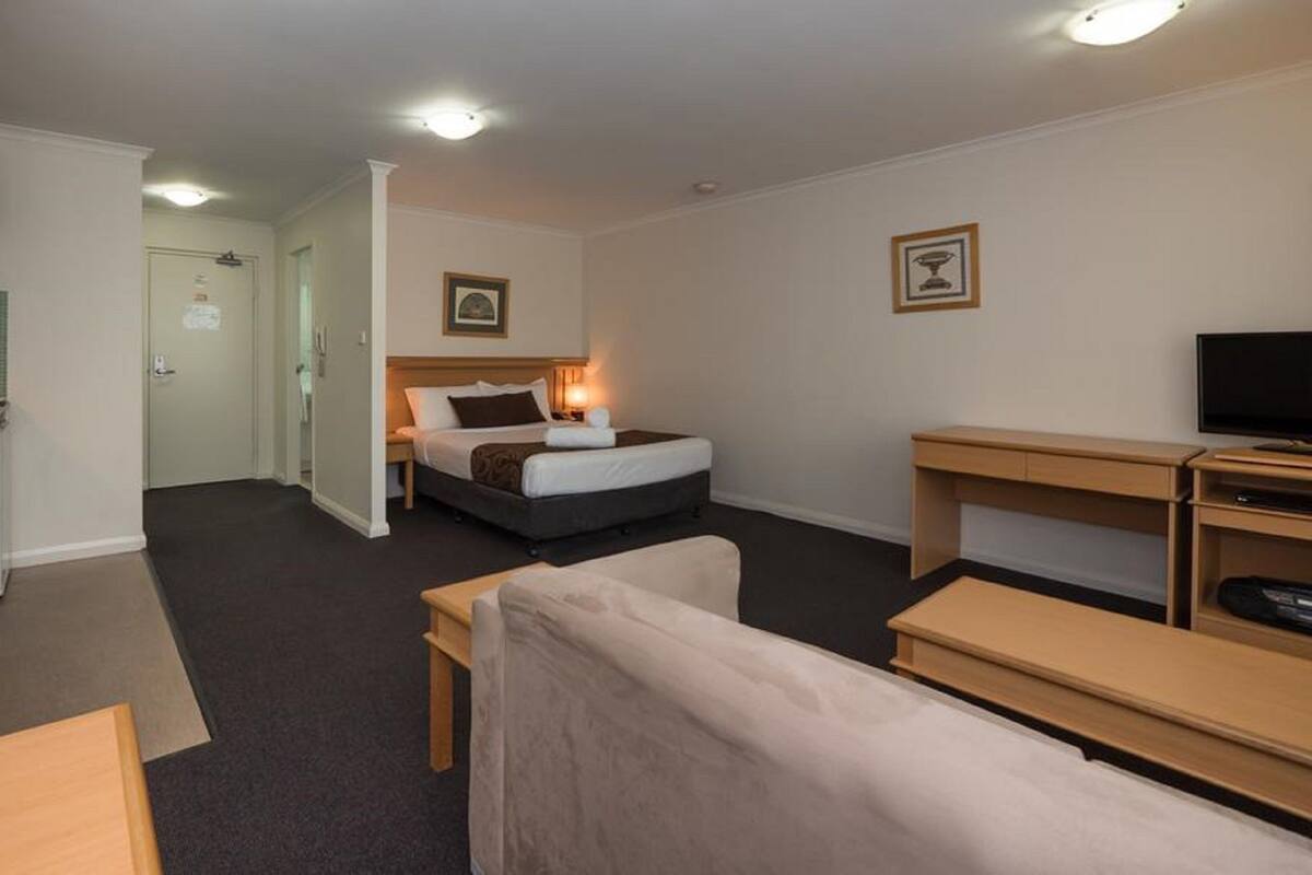 A hotel room with a bed, a desk, a chair, a TV, a kitchenette, and a bathroom.