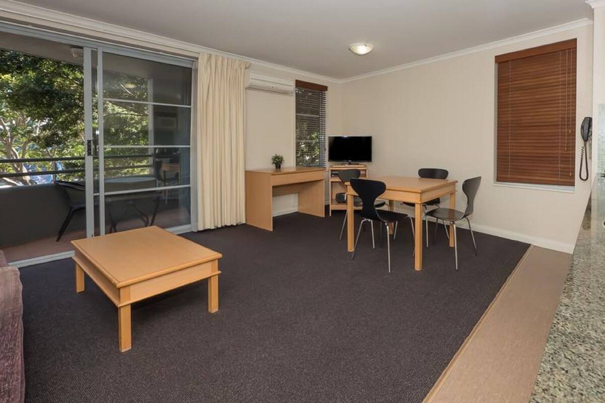 A compact living space with a balcony, a kitchenette, a dining area, and a TV.