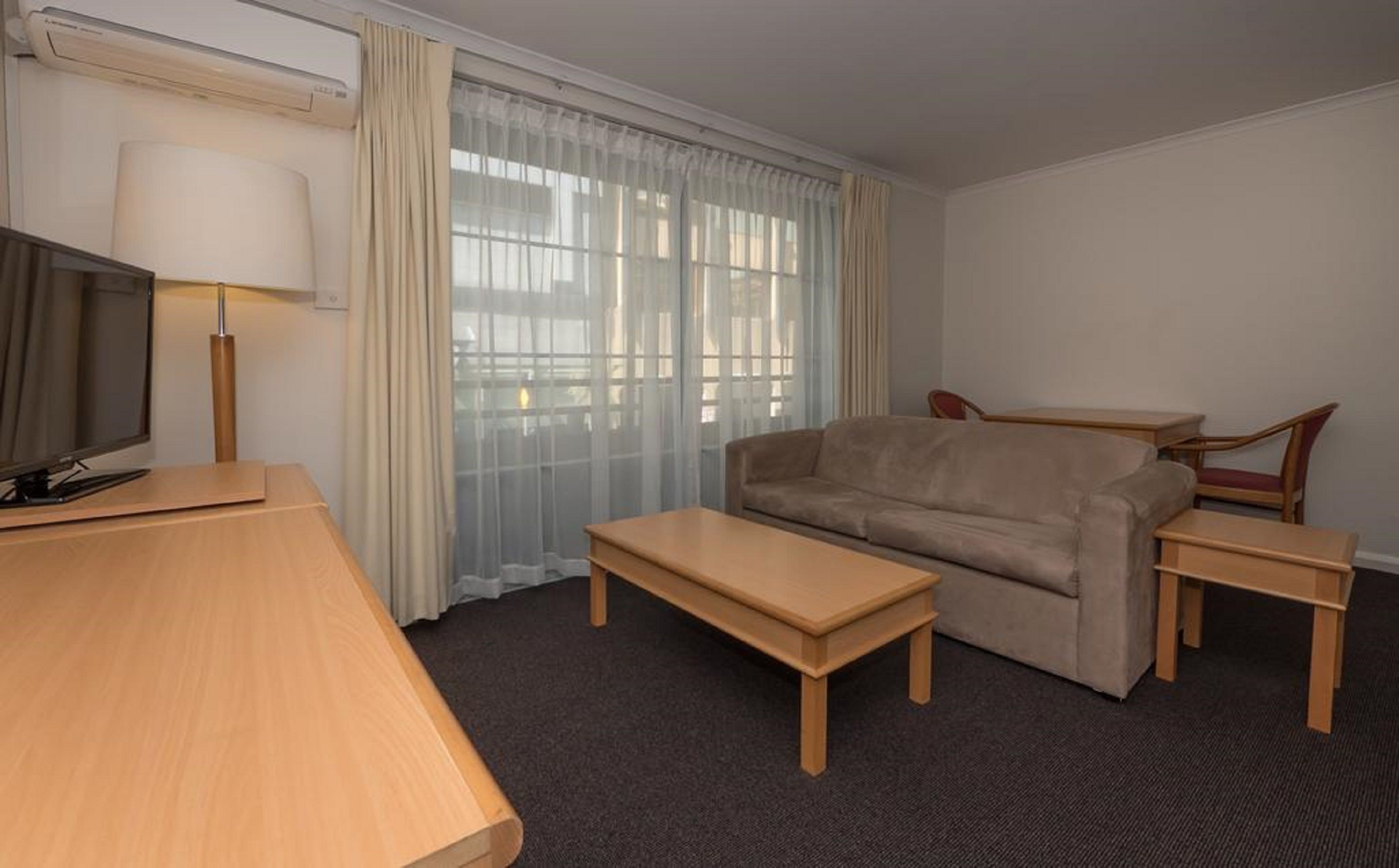 A hotel room with a sofa, a TV, a lamp, a small table, and a chair.