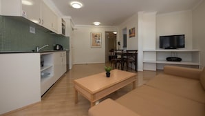 A modern living room with a beige sofa, a wooden coffee table, and a TV on a white shelf.