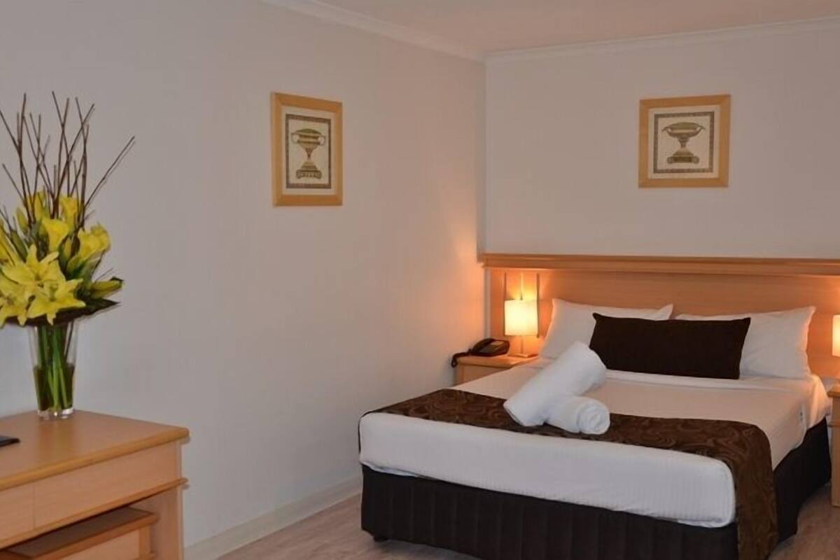 A hotel room with a neatly made bed, bedside tables, a lamp, and a vase of flowers.