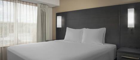 A hotel room with a large bed, a nightstand, and a window with sheer curtains.