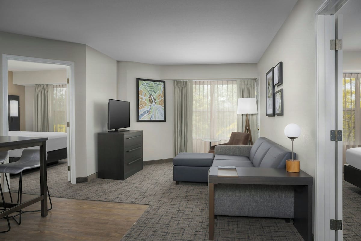 A modern hotel room with a bed, a sofa, a desk, a television, and a large window with curtains.