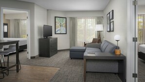 Ett modernt hotellrum med en säng, en soffa, ett skrivbord, en tv och ett stort fönster med gardiner.