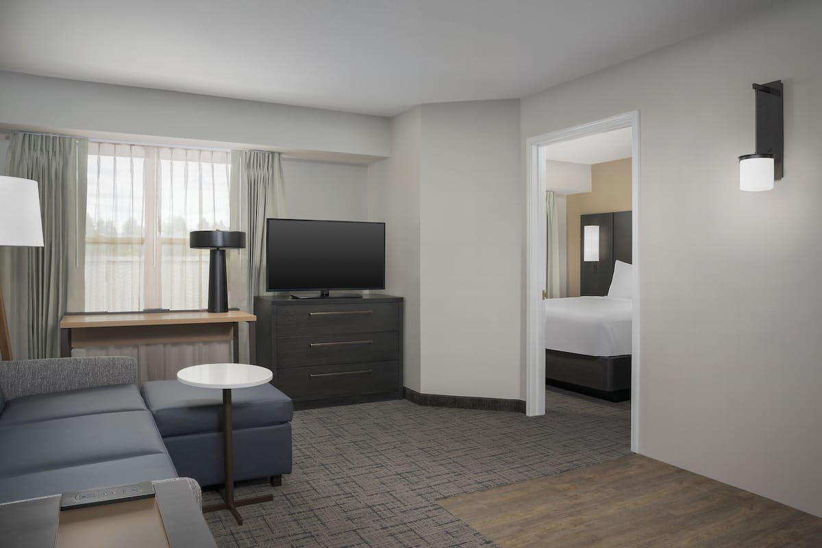 A hotel room with a sofa, a TV, a desk, a bed, and a lamp.
