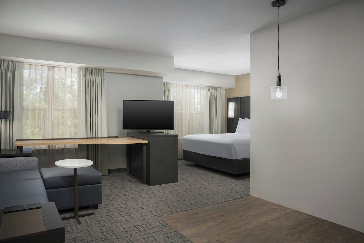A modern hotel room with a bed, a TV, a desk, and a sofa.
