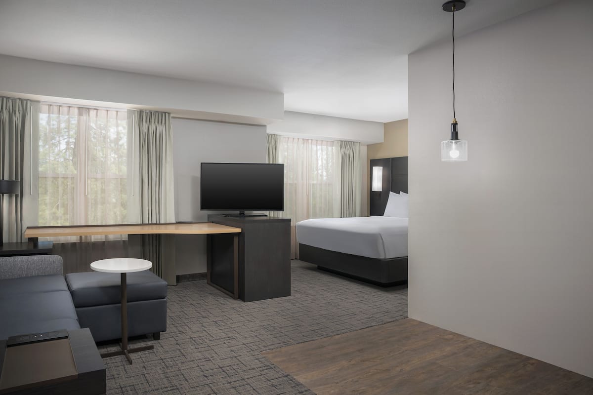 A modern hotel room with a flat-screen TV, a bed, a sofa, a small table, and a desk.