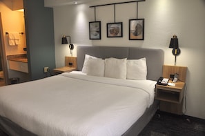 A hotel room with a large bed, two bedside tables, a nightstand, a wall-mounted lamp, and a framed picture above the bed. - Sleep Inn Fort Pierce I-95 (Fort Pierce)
