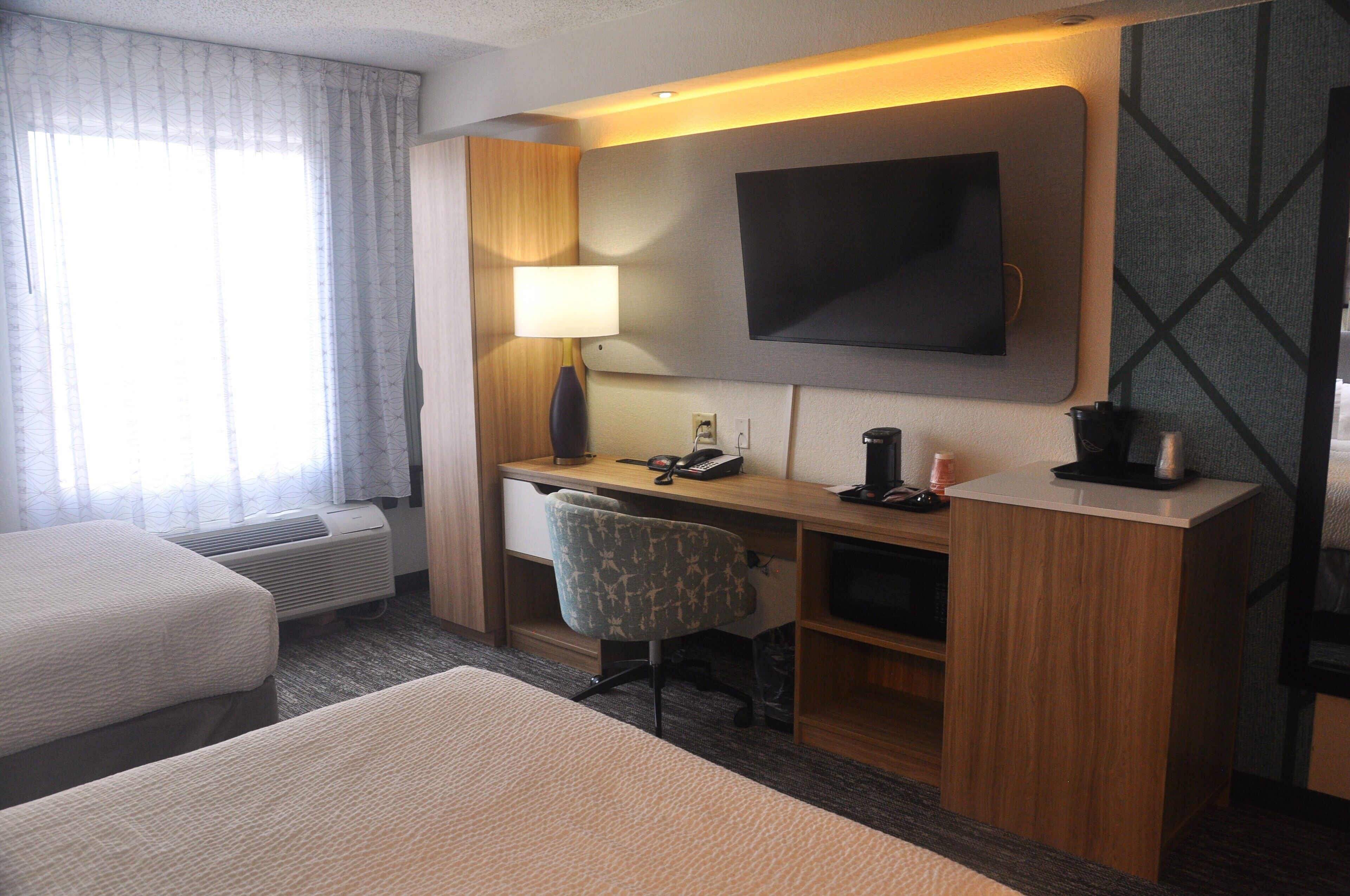 Habitación de hotel con escritorio, silla, televisión y dos camas.