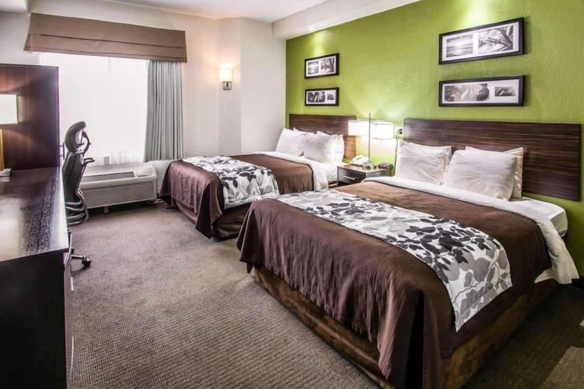 A hotel room with two beds, a desk, a chair, and a window with curtains.