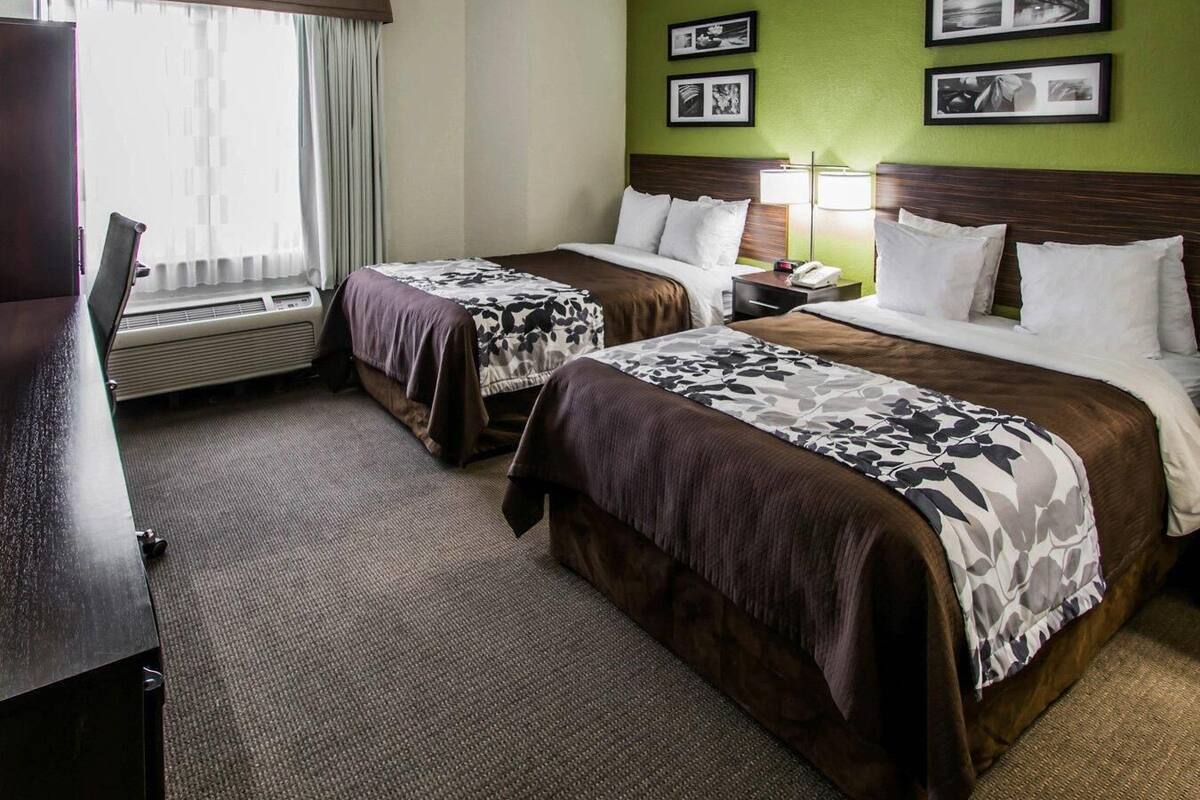A hotel room with two beds, a desk, a chair, a lamp, and a window with curtains.