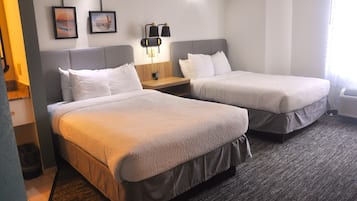 A hotel room with two beds, a nightstand, a lamp, and two framed pictures on the wall.