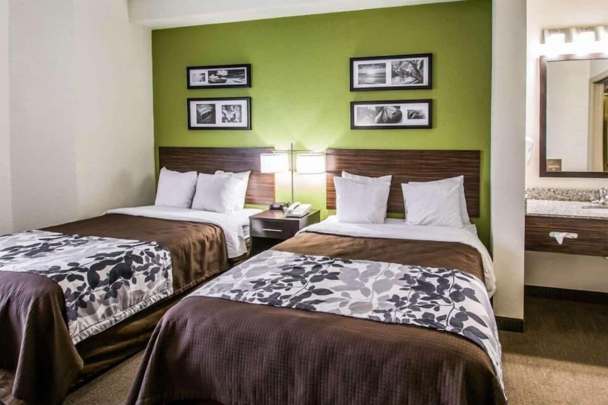 A hotel room with two beds, a green accent wall, framed pictures, a nightstand, and a mirror.